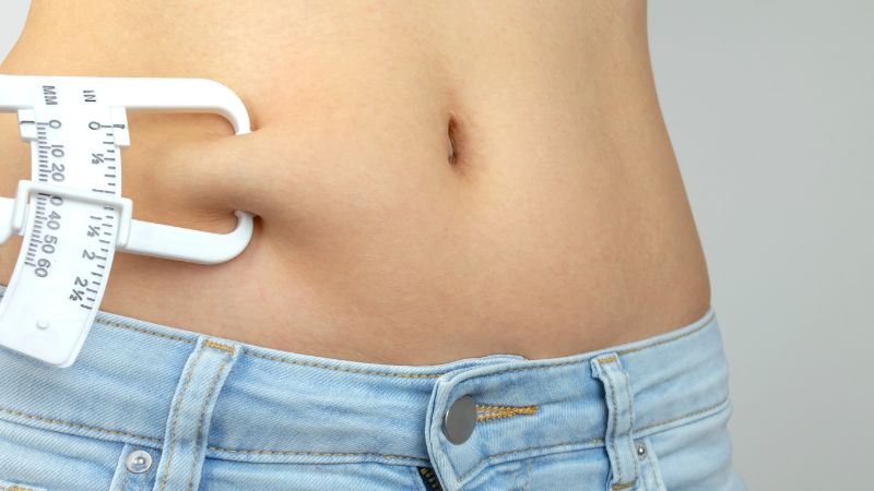 junge frau miss t sich mit einer körperfettzange die fettfalte an ihrer linken hüfte