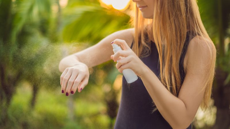 junges mädchen besprüht ihren nackten oberarm mit einem insektenschutzspray